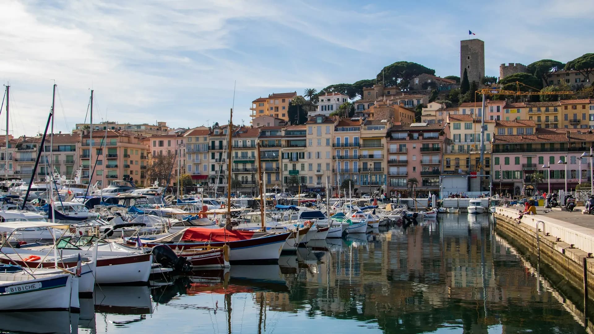 Vieux Port de Cannes avec ses bateaux amarrés, les façades colorées du Suquet et la tour du Suquet en arrière-plan